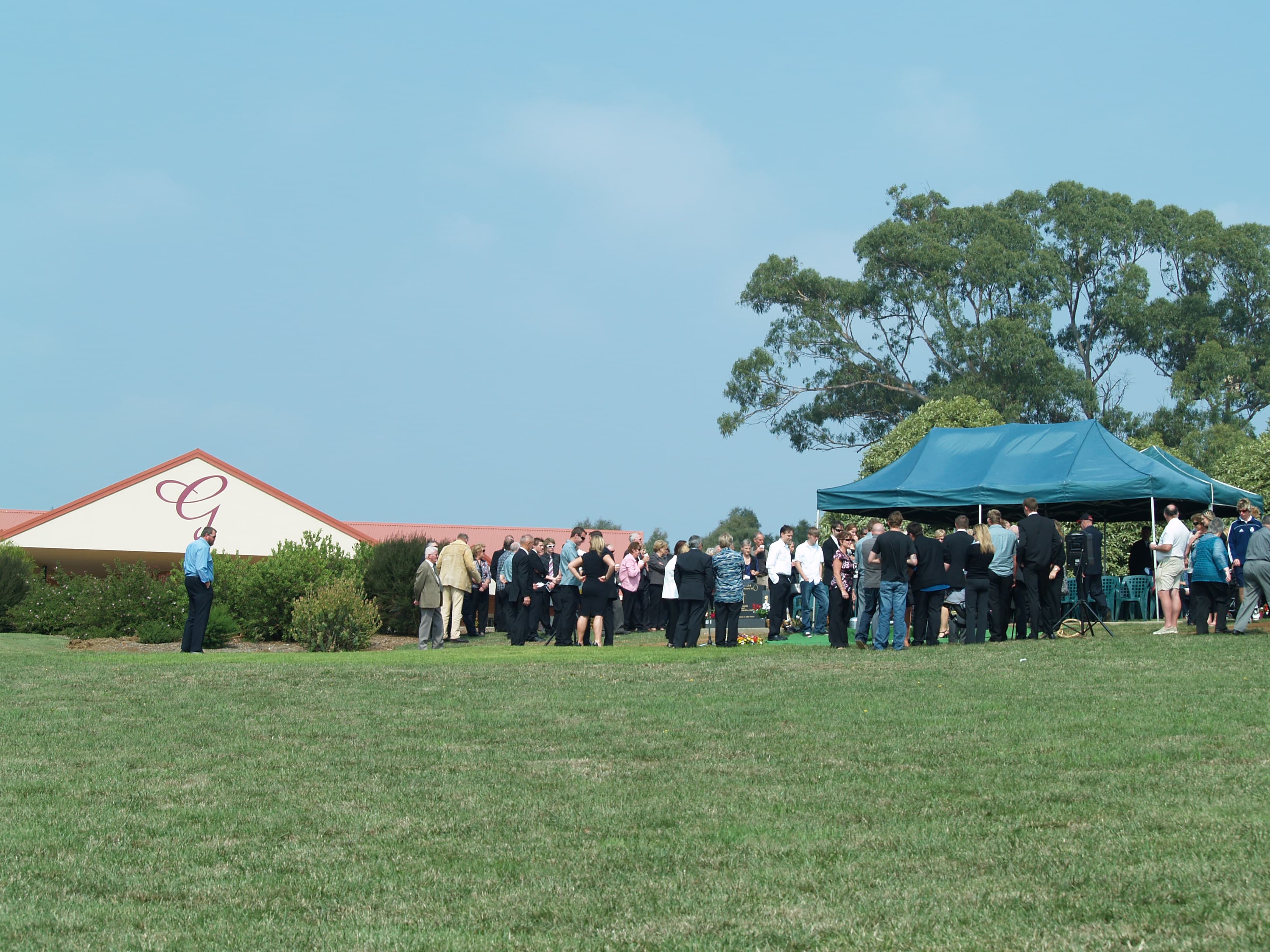 Family and friends gathered under a marquee at a graveside service