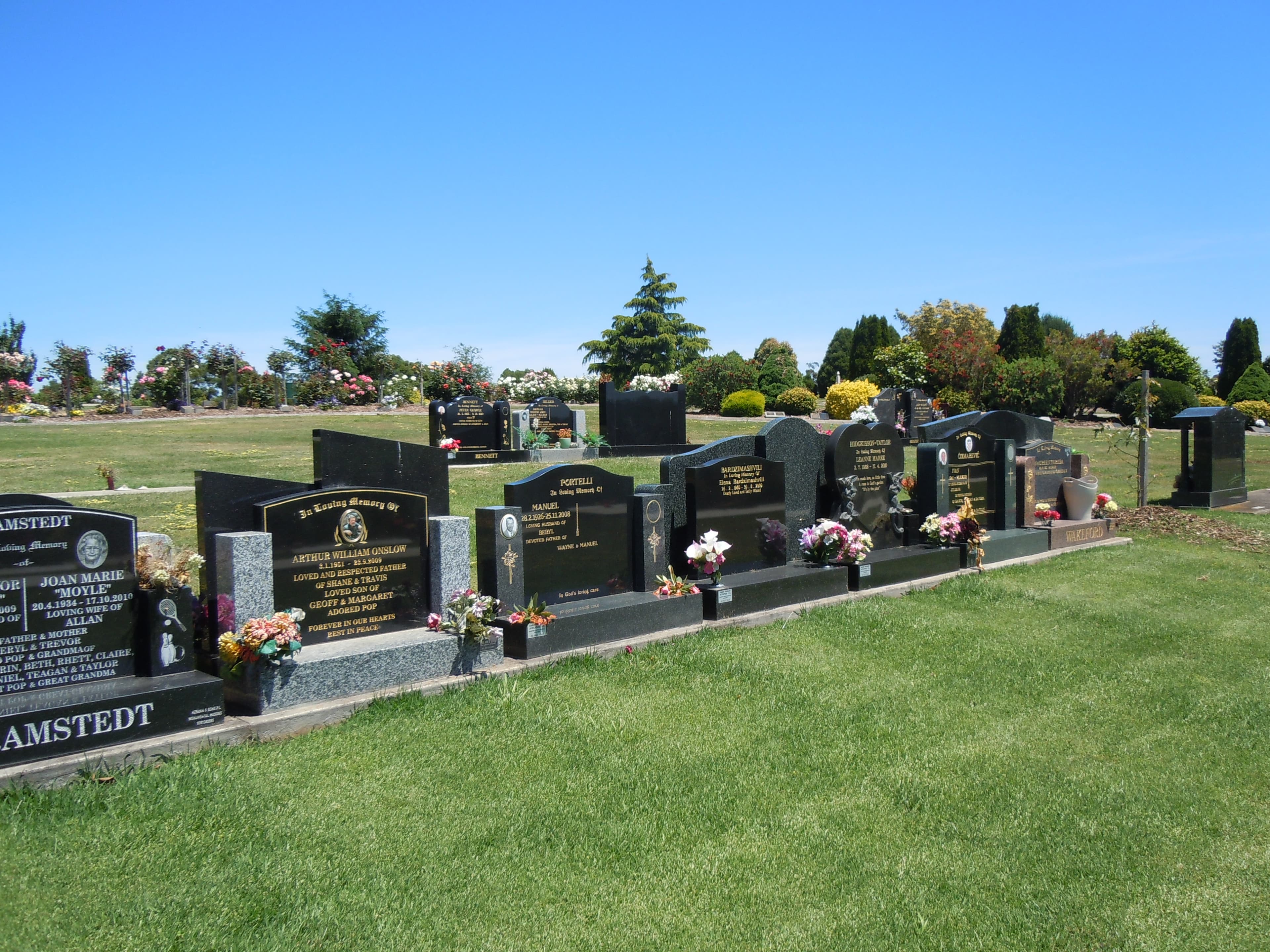 A row of granite headstones with brass plaques in a lawn cemetery