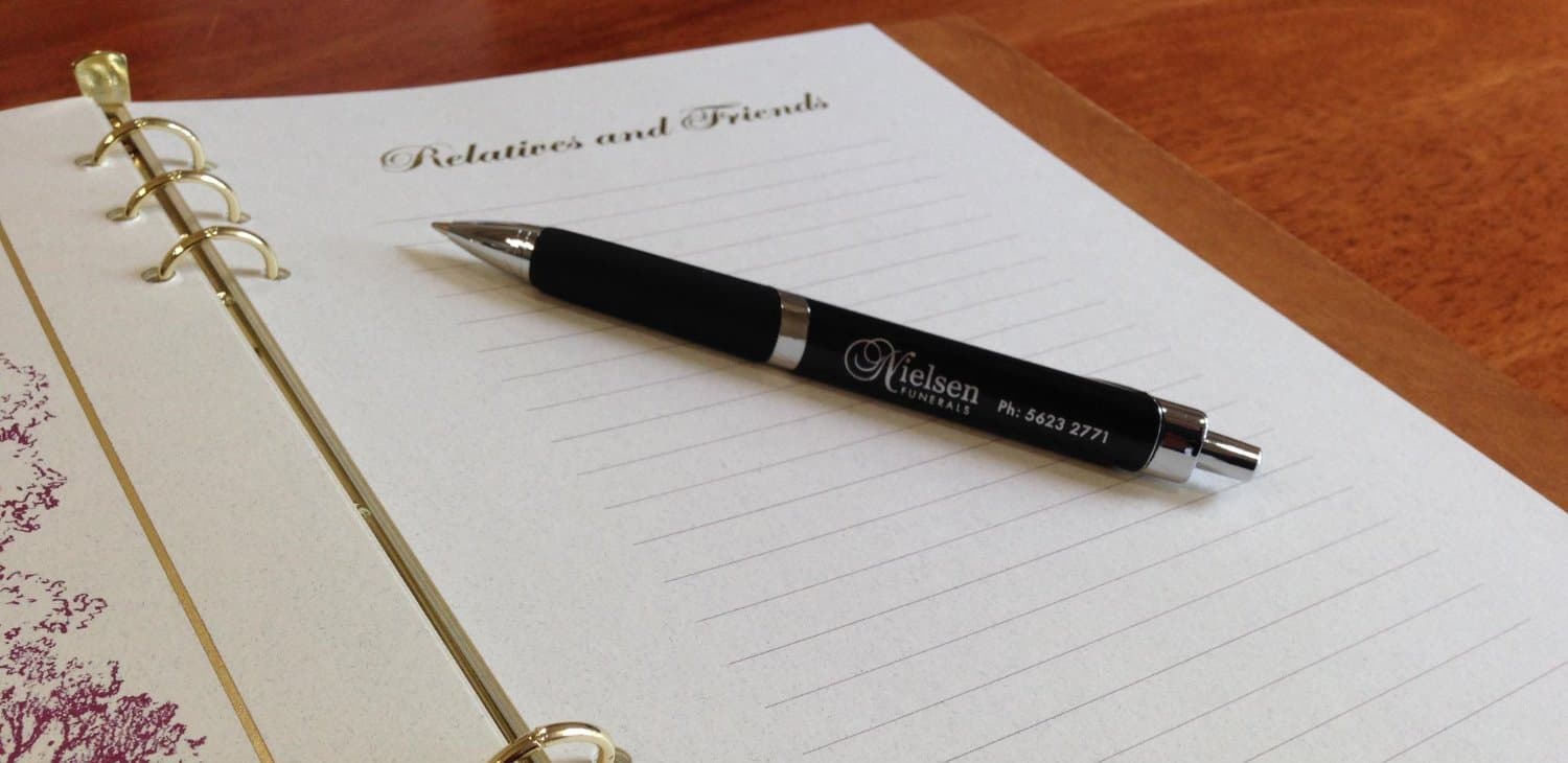 An open memorial book with a Nielsen Funerals pen
