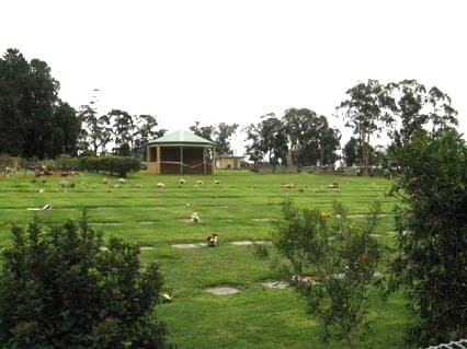 A lawn cemetery with a rotunda and memorial plaques set among gardens
