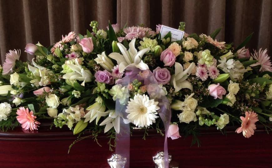 Pink, white and lilac casket spray with lilies, roses and ribbon