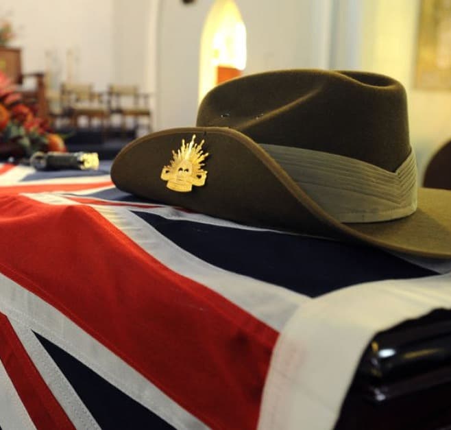 A slouch hat with Rising Sun badge resting on a flag-draped coffin