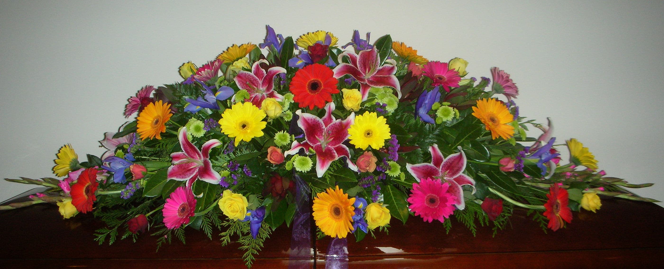 Bright seasonal mixed casket spray with gerberas, lilies and roses